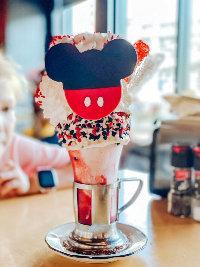 a Crazyshake in a large glass with a sprinkle rim with a mickey decorated Rice Krispie treat