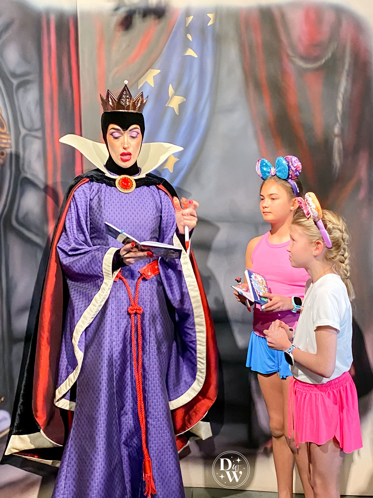 Evil Queen signing an autograph book for two girls at a meet and greet at Disney's Storybook Dining signature character dining experience